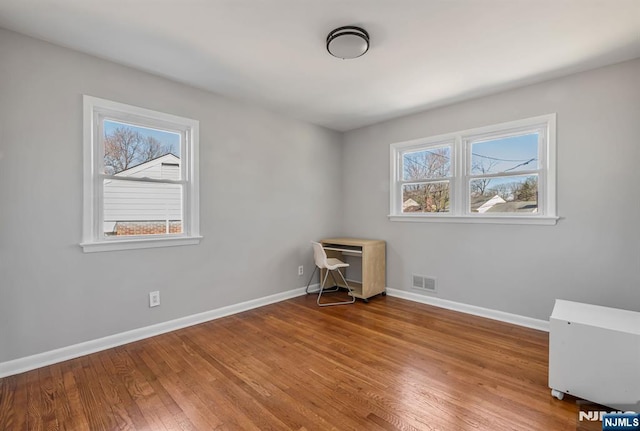 interior space with a wealth of natural light, visible vents, baseboards, and wood finished floors