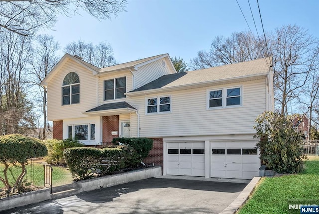 split level home featuring a garage, brick siding, and aphalt driveway