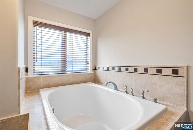 full bathroom featuring tiled bath and lofted ceiling