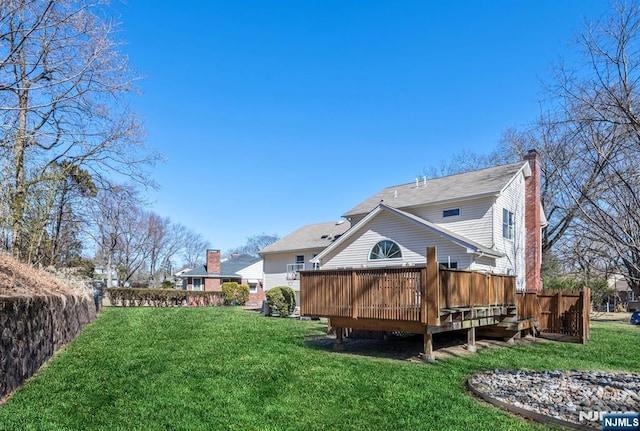 rear view of property with a yard, a wooden deck, a chimney, and fence