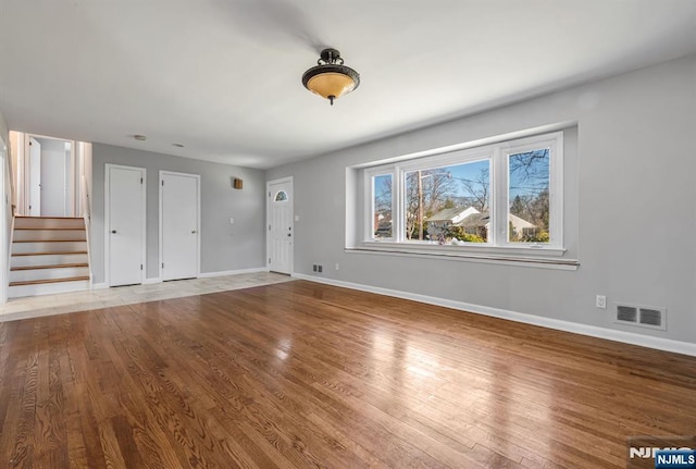 unfurnished living room featuring stairs, wood finished floors, visible vents, and baseboards