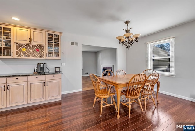 dining space with baseboards, visible vents, dark wood-style flooring, and a lit fireplace