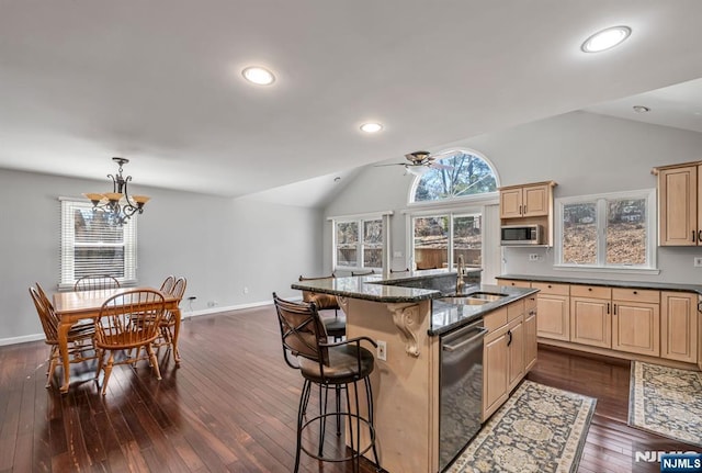 kitchen featuring light brown cabinets, a sink, stainless steel appliances, a breakfast bar area, and vaulted ceiling