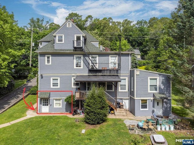 back of property with roof with shingles, a yard, a patio area, a balcony, and stairs