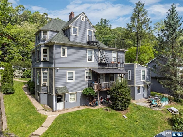 back of house with a chimney, a shingled roof, a lawn, and a patio area