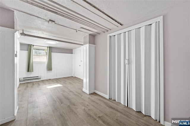 basement featuring a baseboard heating unit, a textured ceiling, and wood finished floors