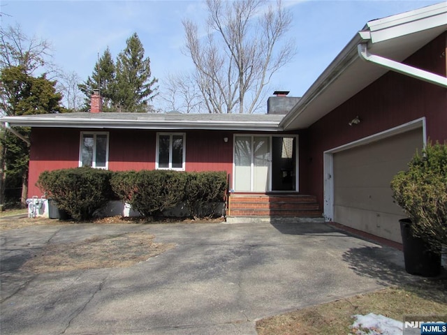 entrance to property featuring a garage, driveway, and a chimney