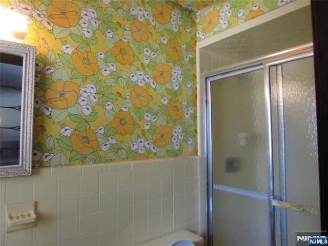 full bathroom featuring tile walls, wainscoting, a shower stall, and wallpapered walls