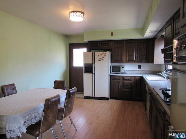 kitchen with light wood-style flooring, dark brown cabinetry, white refrigerator with ice dispenser, a sink, and stainless steel microwave