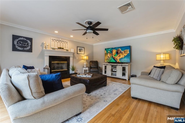 living room featuring visible vents, ornamental molding, wood finished floors, and a glass covered fireplace