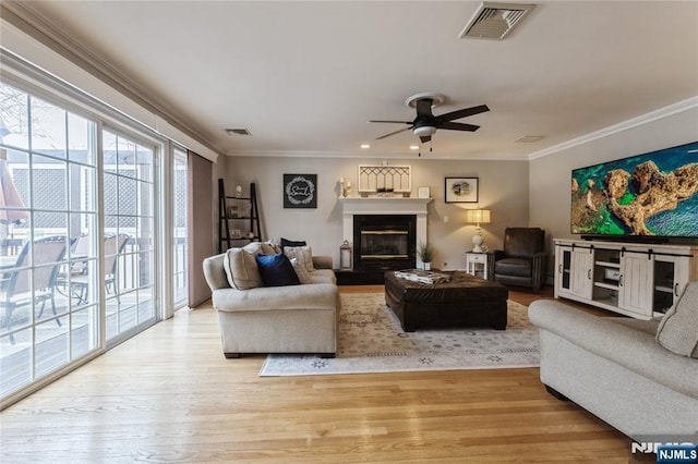 living area with light wood-style floors, a glass covered fireplace, visible vents, and crown molding