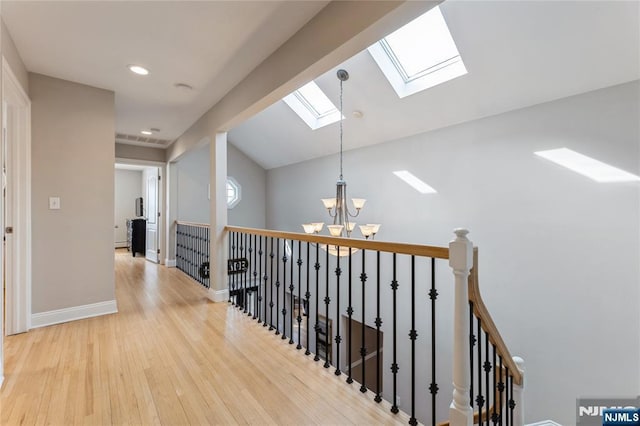 hall featuring a notable chandelier, light wood-style flooring, an upstairs landing, vaulted ceiling with skylight, and baseboards