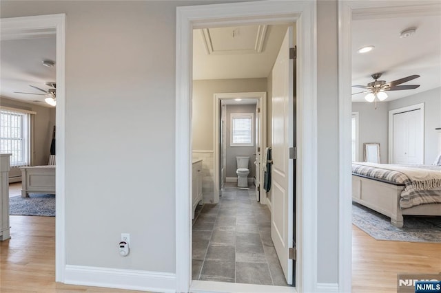 corridor featuring baseboards, wood finished floors, attic access, and a healthy amount of sunlight