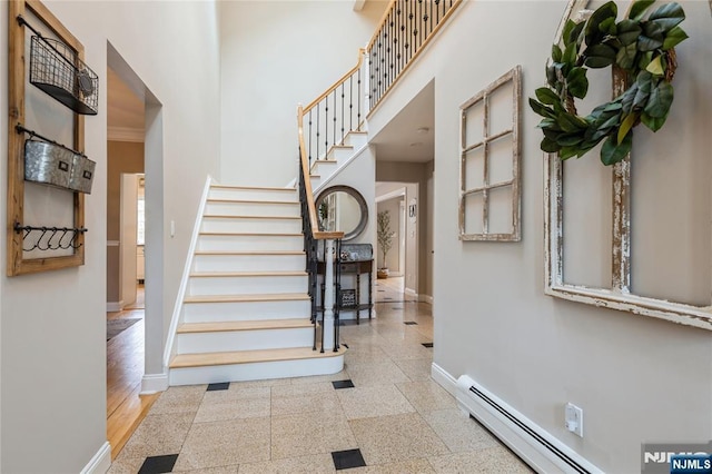 stairway featuring a baseboard heating unit, ornamental molding, a towering ceiling, and baseboards