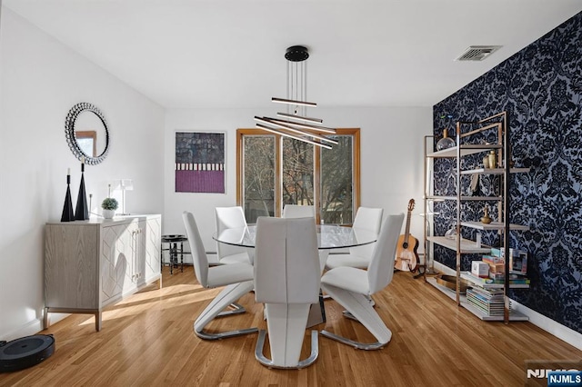 dining area featuring wallpapered walls, an accent wall, visible vents, and wood finished floors