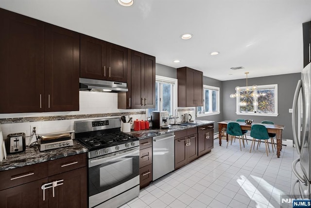 kitchen featuring decorative light fixtures, stainless steel appliances, backsplash, dark brown cabinetry, and under cabinet range hood