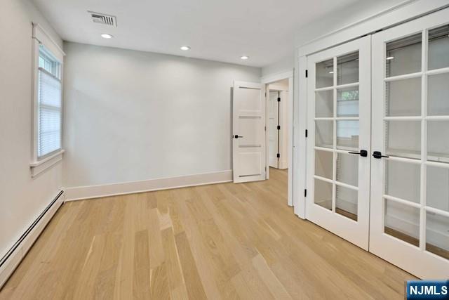 spare room with a baseboard heating unit, visible vents, baseboards, french doors, and light wood-type flooring