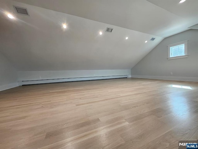 additional living space with vaulted ceiling, a baseboard heating unit, light wood-type flooring, and visible vents