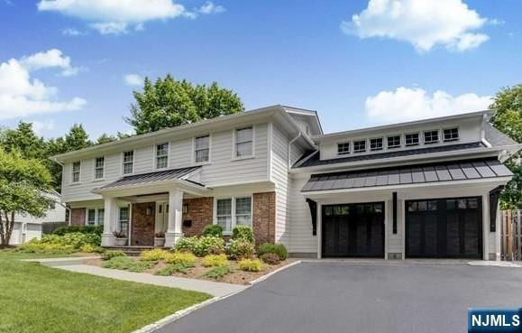 view of front of house featuring aphalt driveway, brick siding, a standing seam roof, metal roof, and a front lawn