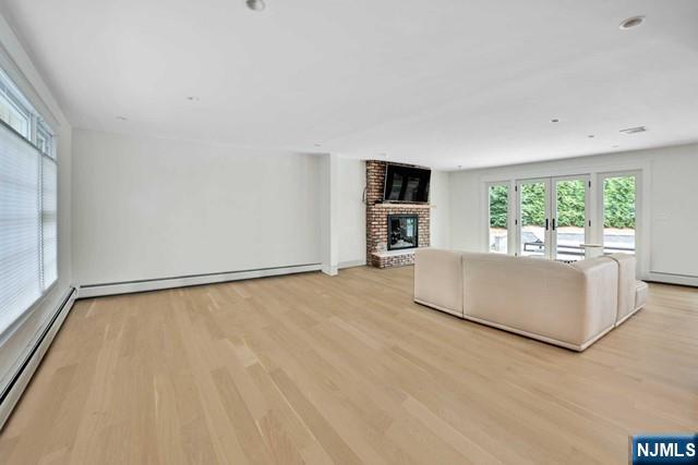 unfurnished living room featuring a brick fireplace, baseboard heating, light wood-style floors, and french doors