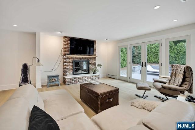 living area featuring a baseboard radiator, wood finished floors, french doors, a brick fireplace, and recessed lighting