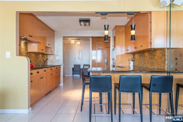 kitchen featuring paneled refrigerator, dark countertops, a peninsula, light tile patterned flooring, and decorative backsplash