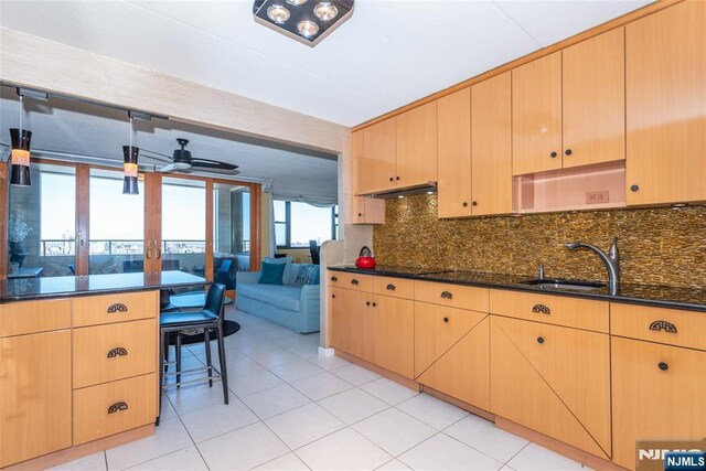 kitchen featuring dark stone countertops, light brown cabinets, a sink, under cabinet range hood, and tasteful backsplash