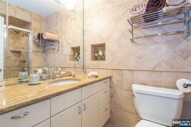 full bathroom featuring vanity, tile walls, toilet, and tiled shower