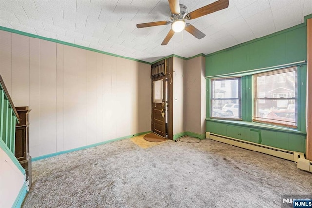 carpeted spare room featuring crown molding, stairway, baseboard heating, a ceiling fan, and baseboards