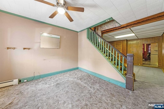 carpeted spare room featuring a ceiling fan, wood walls, and stairs