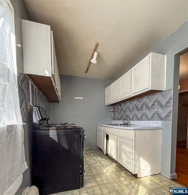 kitchen with a sink, decorative backsplash, stove, light countertops, and white cabinetry