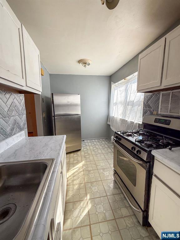 kitchen with a sink, white cabinets, backsplash, and stainless steel appliances