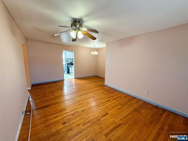 spare room with ceiling fan with notable chandelier, baseboards, and light wood-style floors