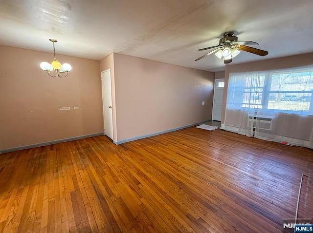 empty room featuring hardwood / wood-style floors, ceiling fan with notable chandelier, and baseboards