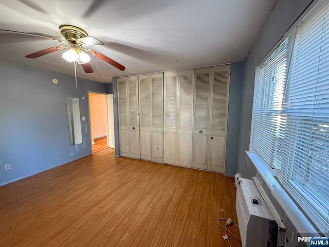 unfurnished bedroom with ceiling fan, wood finished floors, and a wall mounted AC