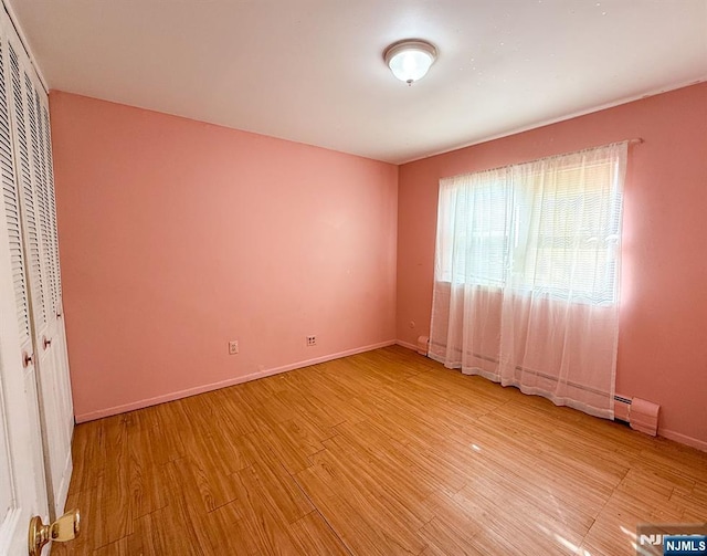 unfurnished bedroom featuring a closet, light wood-type flooring, baseboards, and a baseboard radiator