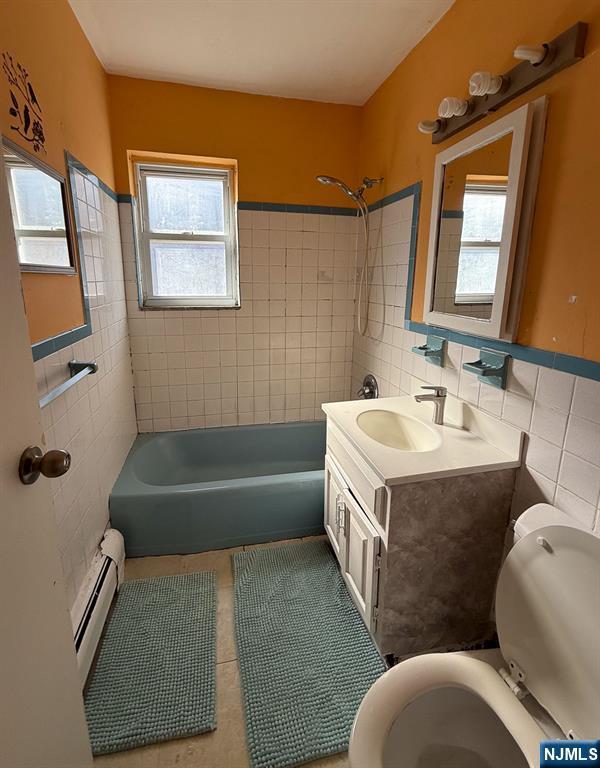 bathroom featuring washtub / shower combination, tile patterned flooring, a baseboard heating unit, tile walls, and toilet