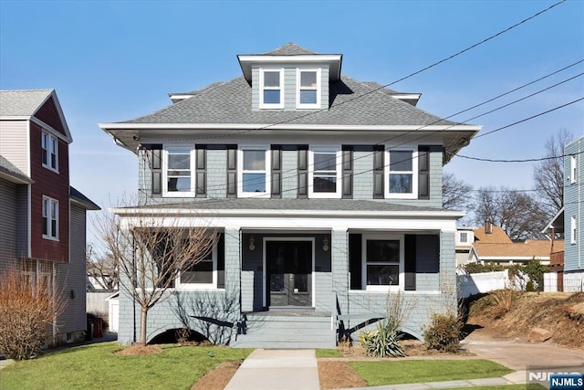 american foursquare style home featuring a porch, a front lawn, and a shingled roof