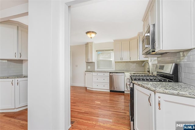 kitchen featuring stainless steel appliances, visible vents, backsplash, light stone countertops, and light wood finished floors