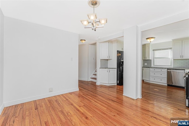 unfurnished living room with baseboards, light wood finished floors, stairway, and an inviting chandelier