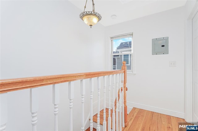 corridor featuring an upstairs landing, baseboards, vaulted ceiling, light wood-type flooring, and electric panel