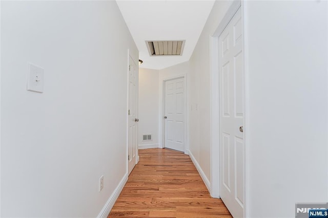 hallway featuring light wood-style floors, baseboards, and visible vents