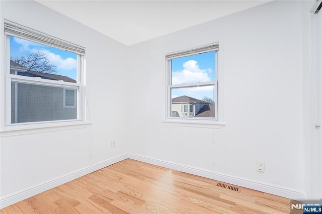 unfurnished room with a healthy amount of sunlight, baseboards, visible vents, and wood finished floors