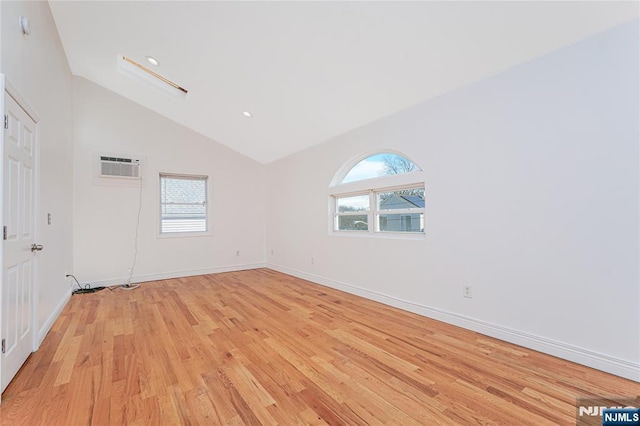 unfurnished room featuring light wood-style flooring, a wall mounted air conditioner, a wealth of natural light, and baseboards