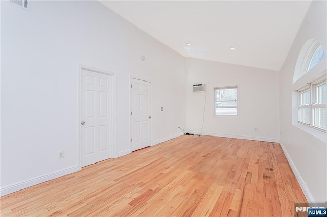 empty room featuring high vaulted ceiling, light wood-style flooring, and baseboards