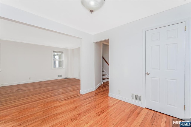 empty room with stairs, light wood finished floors, visible vents, and baseboards