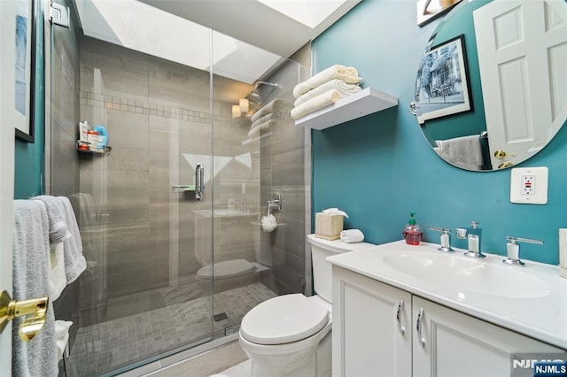 bathroom with toilet, a skylight, a stall shower, and vanity