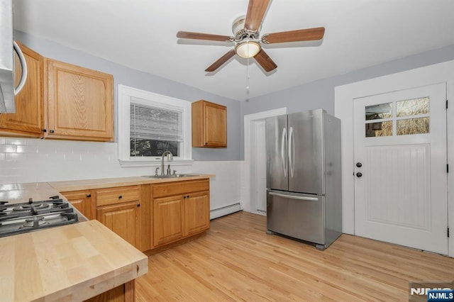 kitchen featuring a baseboard radiator, light wood-style flooring, stainless steel appliances, a sink, and backsplash