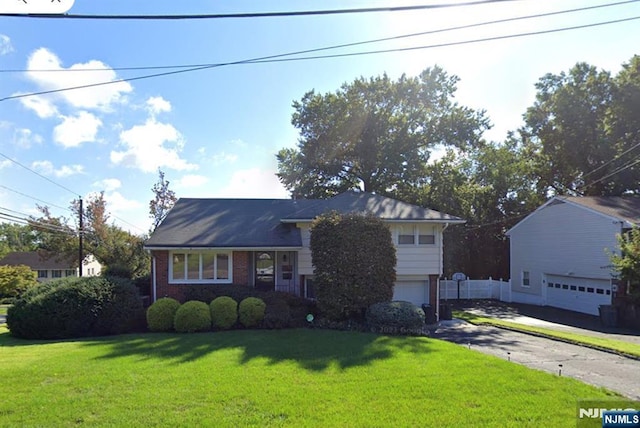 split level home featuring brick siding, an attached garage, fence, driveway, and a front lawn