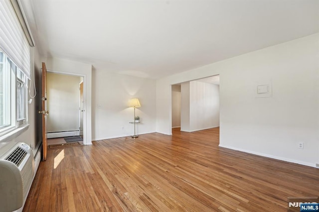 unfurnished living room with a baseboard heating unit, an AC wall unit, light wood-type flooring, and baseboards